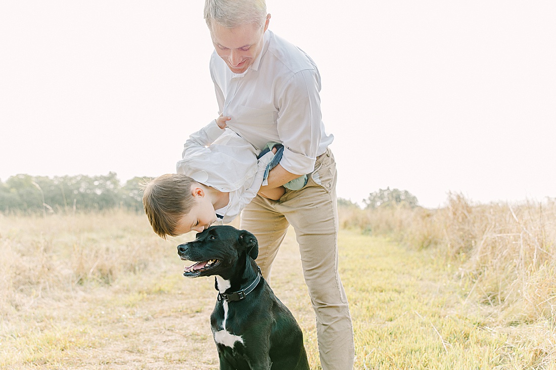 dad hold son upside down as he kisses dog during family photo session with Sara Sniderman Photography in Needham Massachusetts