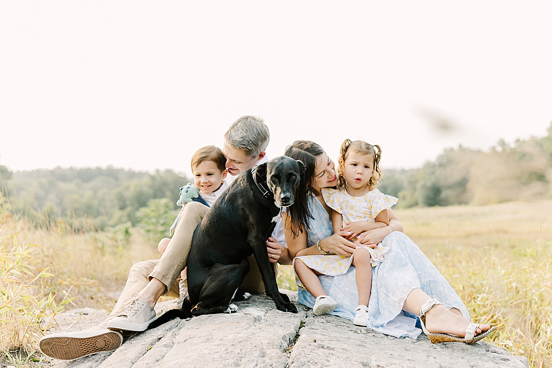 family and dog cuddle on a rock during family photo session with Sara Sniderman Photography in Needham Massachusetts