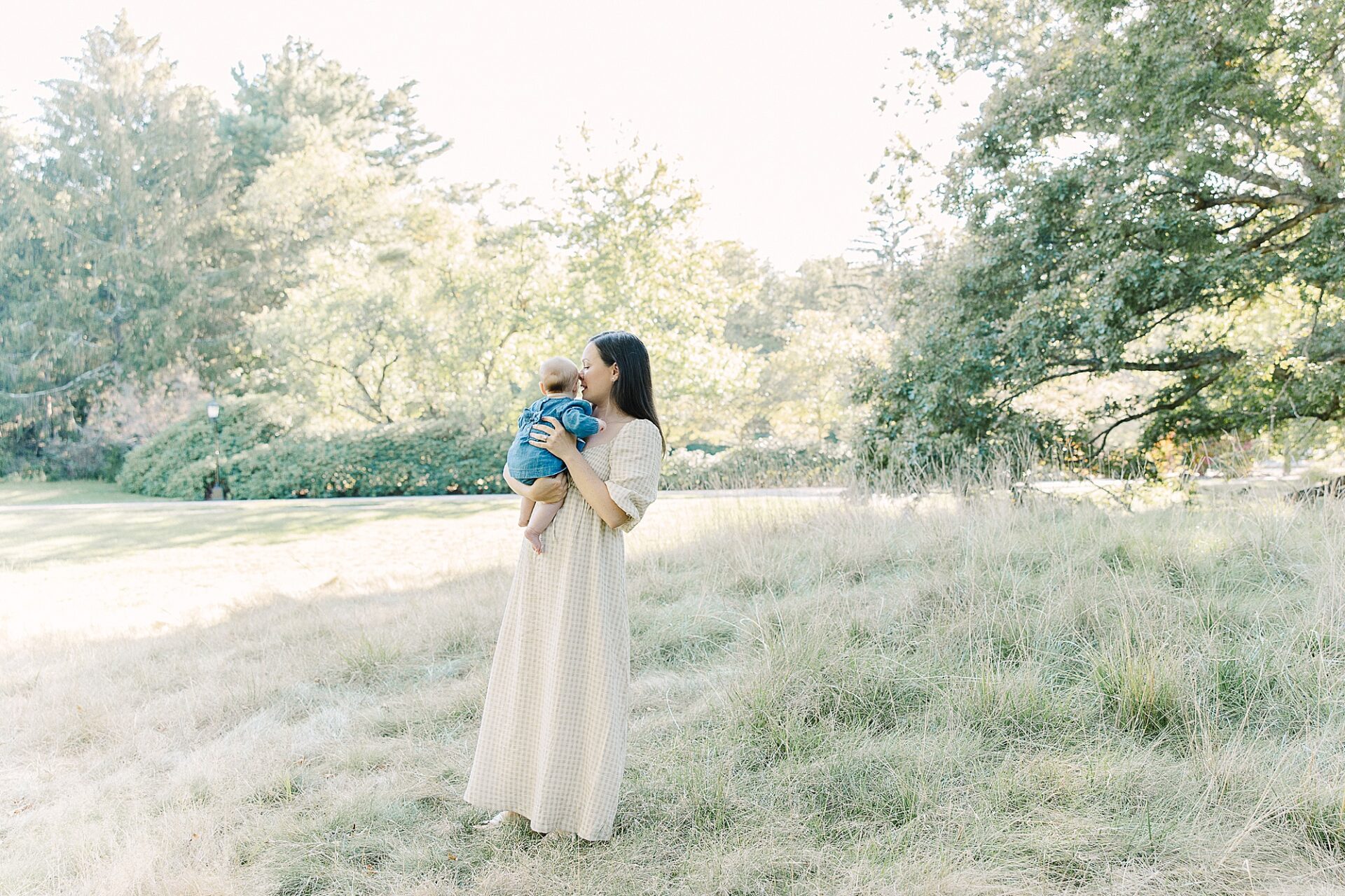 mother stands in field with baby during outdoor newborn photo session with Sara Sniderman Photography at Wellesley College