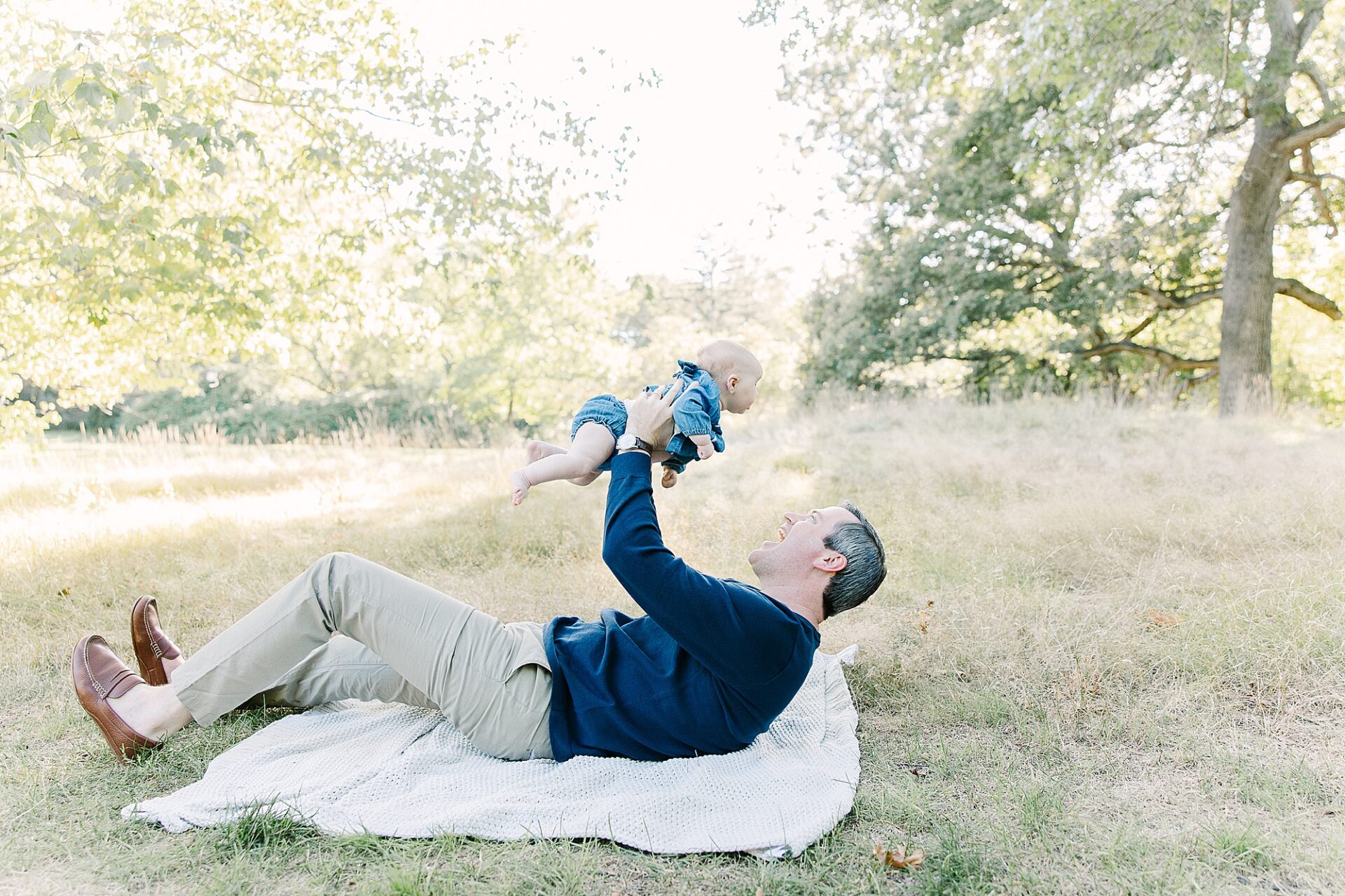 father lays on blanket holding baby above him during outdoor newborn photo session with Sara Sniderman Photography at Wellesley College