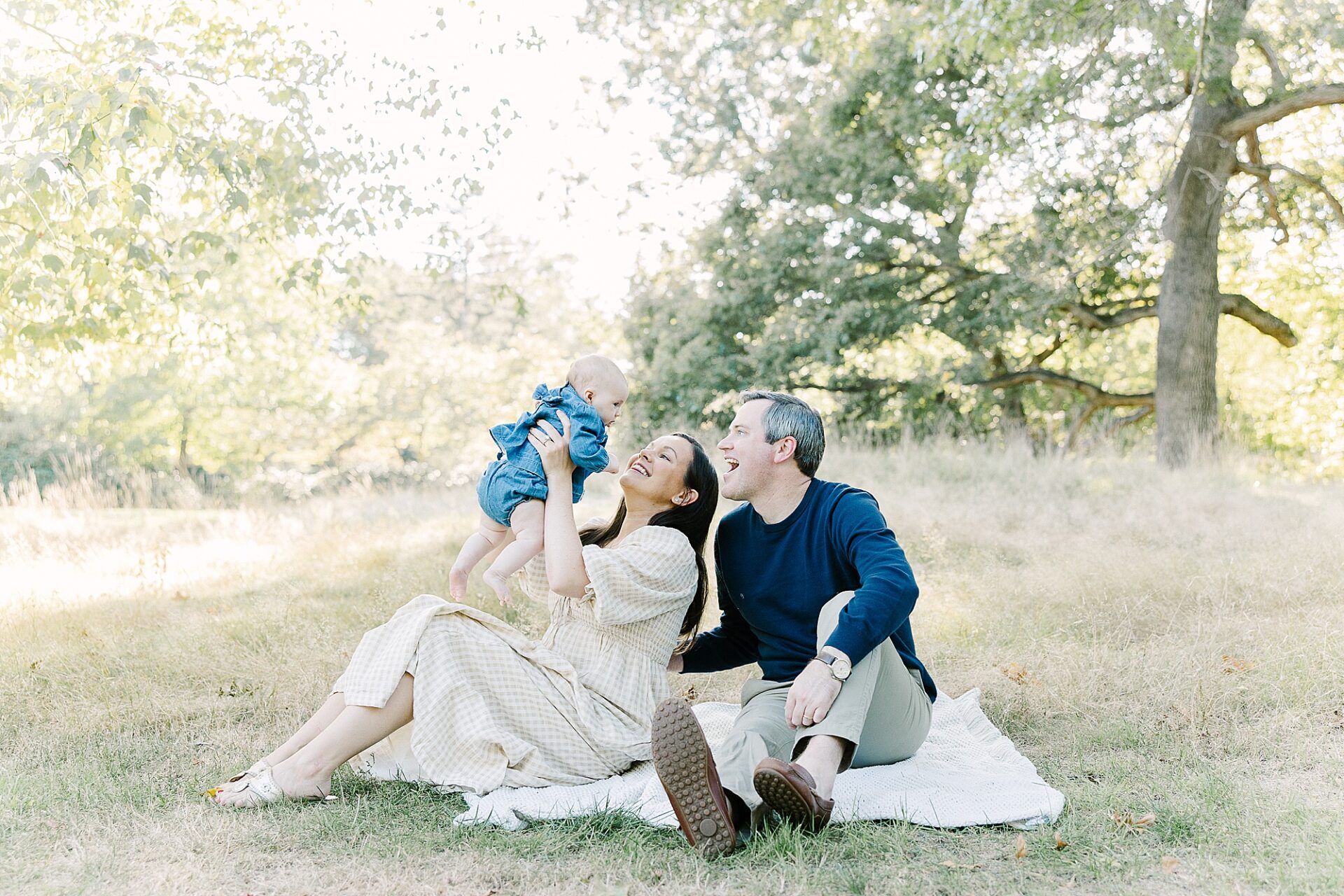 family sits on blanket during outdoor newborn photo session with Sara Sniderman Photography at Wellesley College
