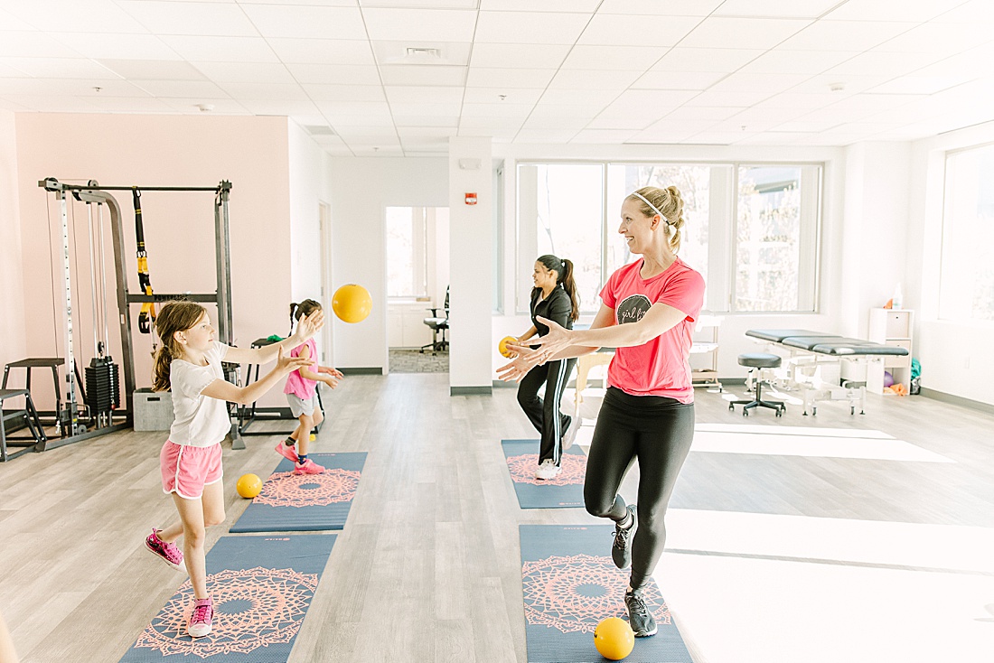 woman and girl throw balls during exercise class at girl fit physical therapy in framingham massachusetts