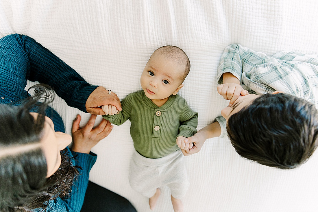 father and toddler lay on bed with baby during in-home newborn photo session with Photographer Sara Sniderman in Metro West Boston. 