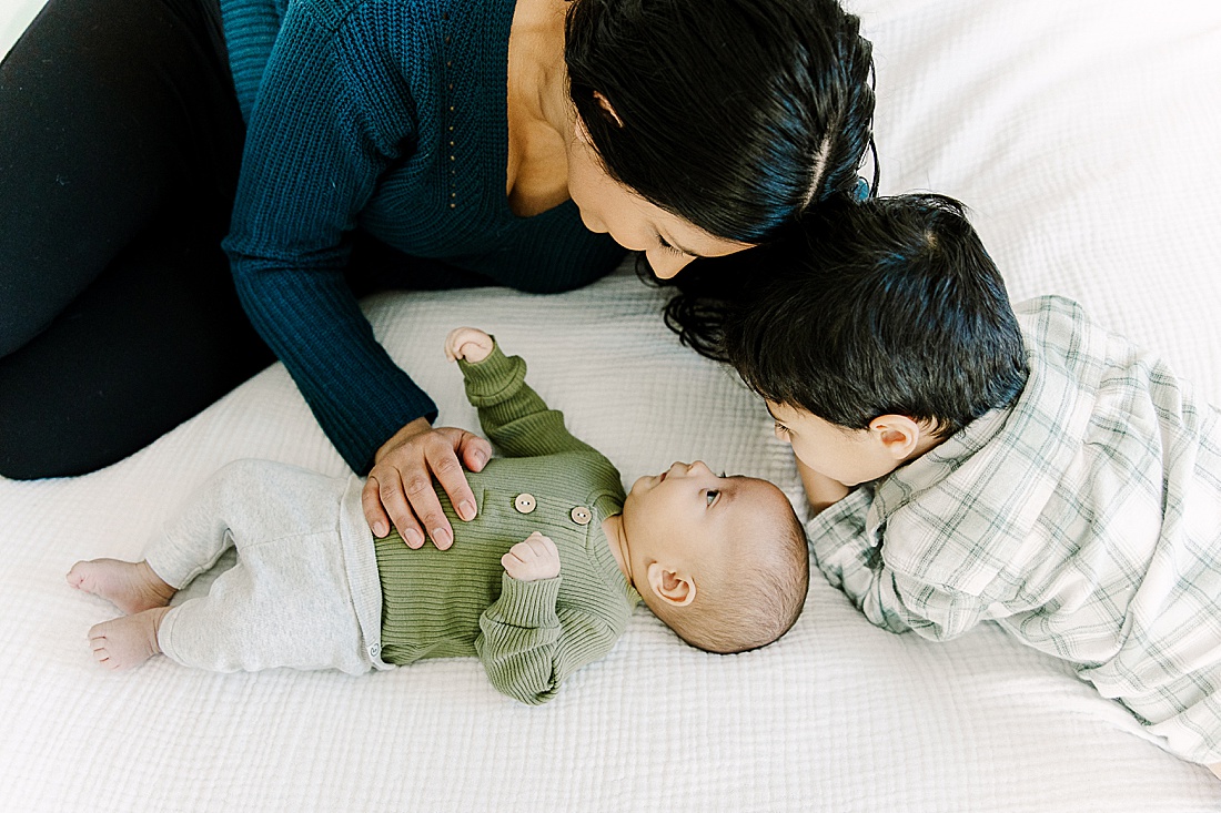 Mother and son lay on bed with baby during in-home newborn photo session with Photographer Sara Sniderman in Metro West Boston.
