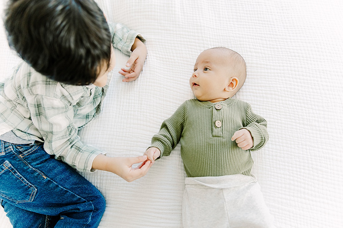 big brother holds babies hand during in-home newborn photo session with Photographer Sara Sniderman in Metro West Boston. 