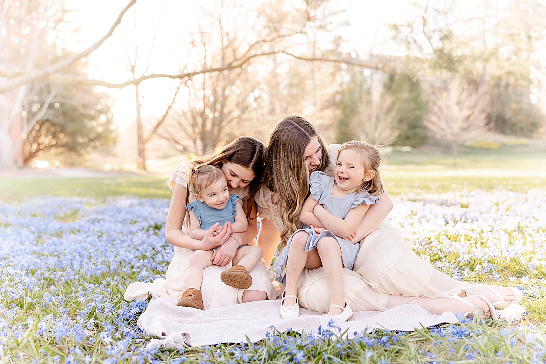 sisters sit in field of flowers during maternity photo session at Wellesley College with Sara Sniderman Photography